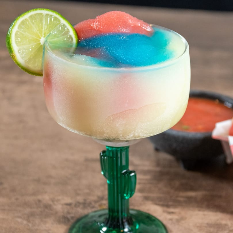 A colorful frozen margarita with red, white, and blue layers, garnished with a lime slice.