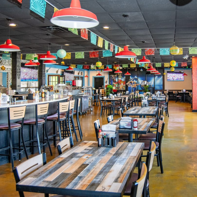 Spacious interior of Reyes Mexican Grill, featuring colorful papel picado, red pendant lights, and rustic wooden tables.