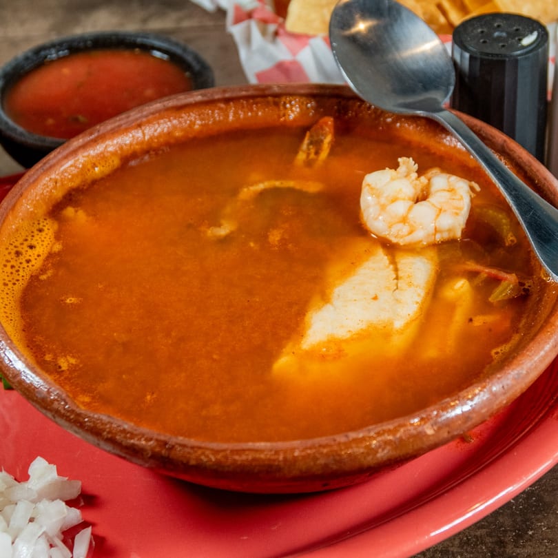 Close-up of a large bowl of red Mexican seafood soup with shrimp and fish.