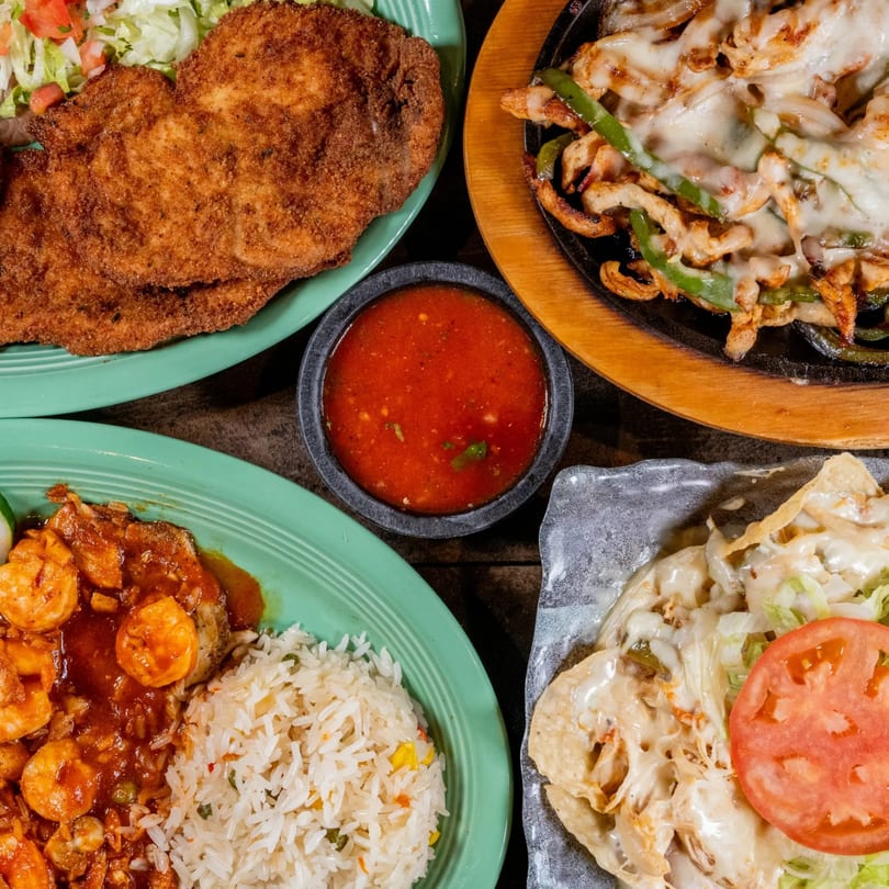 A top-down view of four vibrant Mexican dishes, including fajitas, breaded cutlets, shrimp, and nachos.