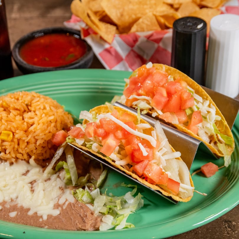 Two Reyes Mexican Grill tacos with rice and beans, salsa, and chips on a green plate.