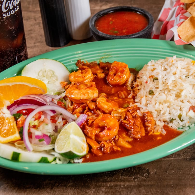 Reyes Mexican Grill's shrimp dish with rice, salad, orange, cucumber, and lime on a green plate.