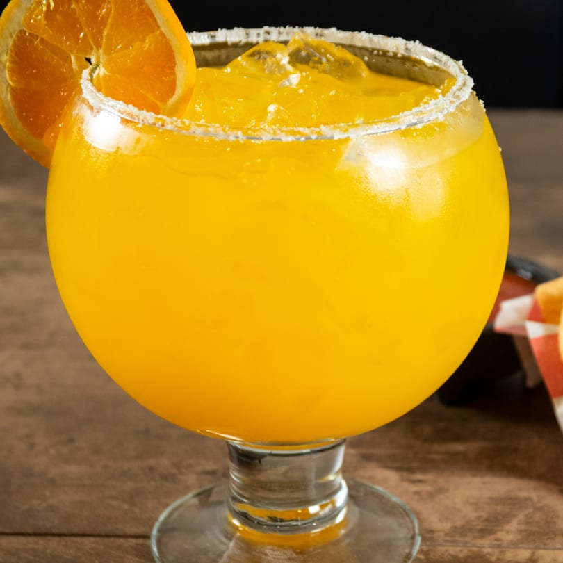 A vibrant orange Reyes Mexican Grill margarita with a salted rim and orange slice garnish.