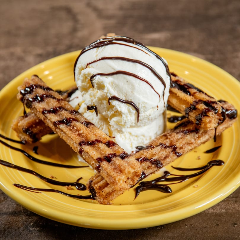 Churros with vanilla ice cream and chocolate syrup on a yellow plate at Reyes Mexican Grill.