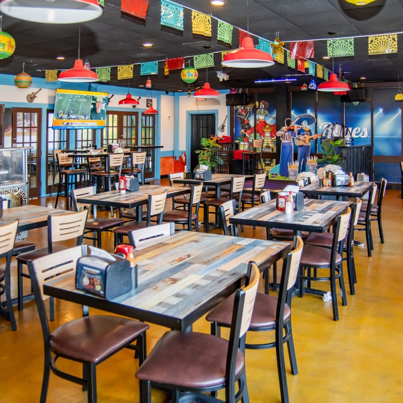 Vibrant interior of Reyes Mexican Grill with colorful papel picado, red lamps, and rustic wooden tables.