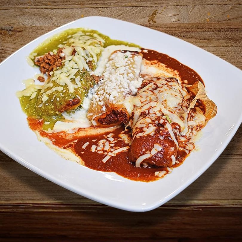 A white plate of Reyes Mexican Grill enchiladas, one with green sauce, one with white sauce, and one with red sauce.